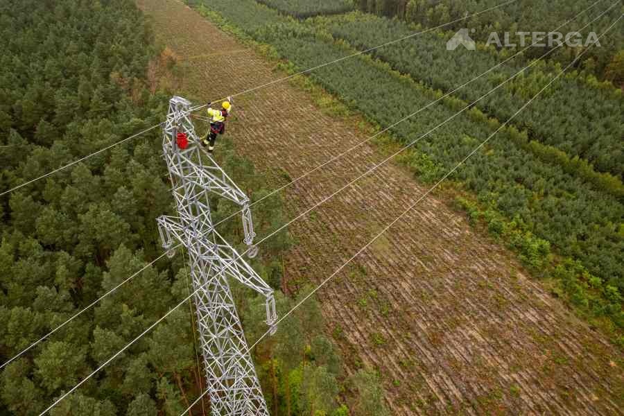 mężczyźni w żółtych kaskach na słupie wysokiego napięcia nad polami
